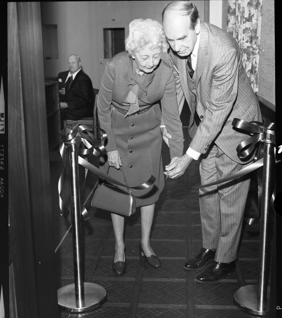 An older woman and man cut a ribbon in a doorframe.