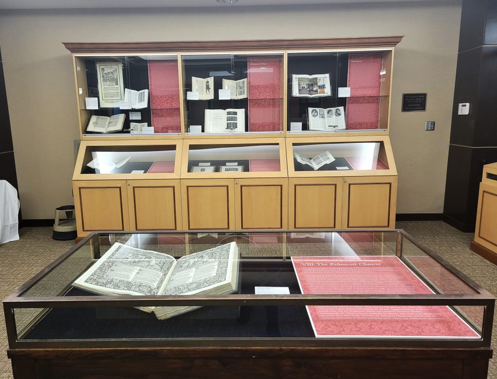 Photograph of a portion of the Art and Labor exhibition that features a display case holding one oversize book in the foreground, and three tall display cases filled with exhibition items in the background. 